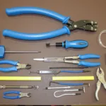 A variety of car trim tools laid out on a workbench, including plastic pry tools, metal pry bars, panel removal tools, and fastener removers.